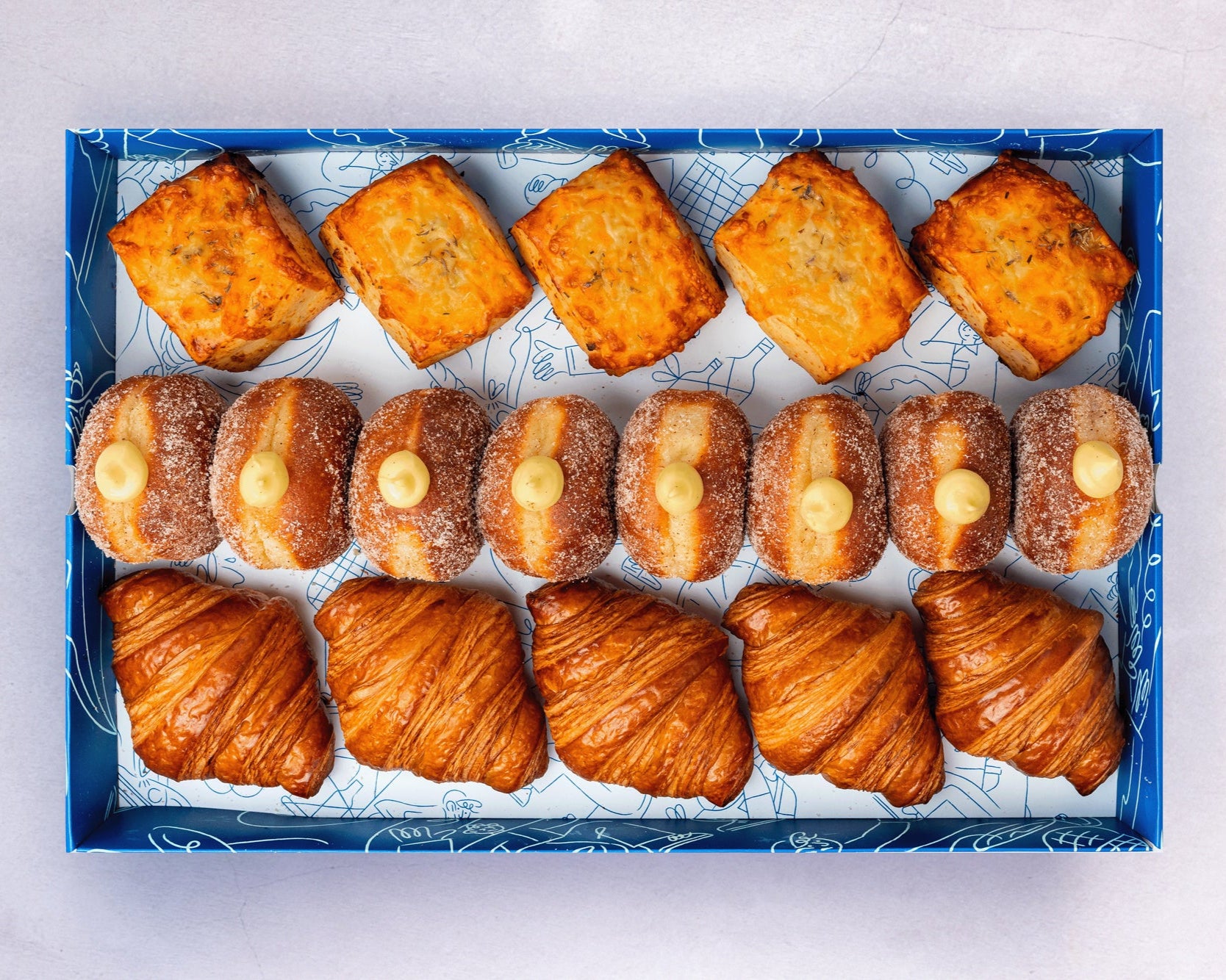 A catering pastry box with a selection of mini croissants, doughnuts, scones, Danishes, and cookies.