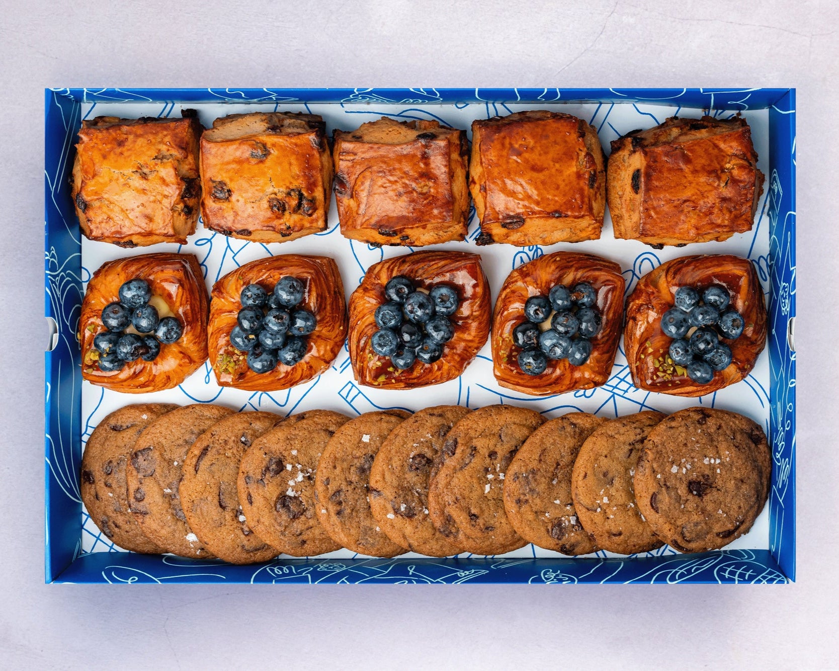 A box of Bakehouse Occasions afternoon tea treats with apple & raisin scones, mini blueberry danish, and chocolate sea salt cookies.